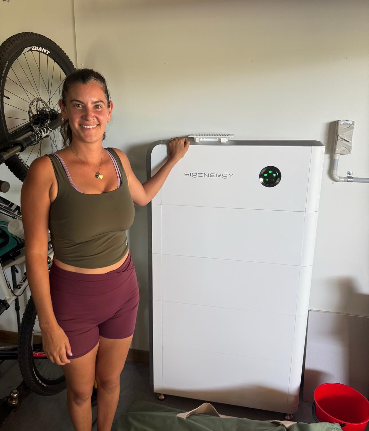 A happy Tidy Energy customer beside her newly installed home battery in her garage
